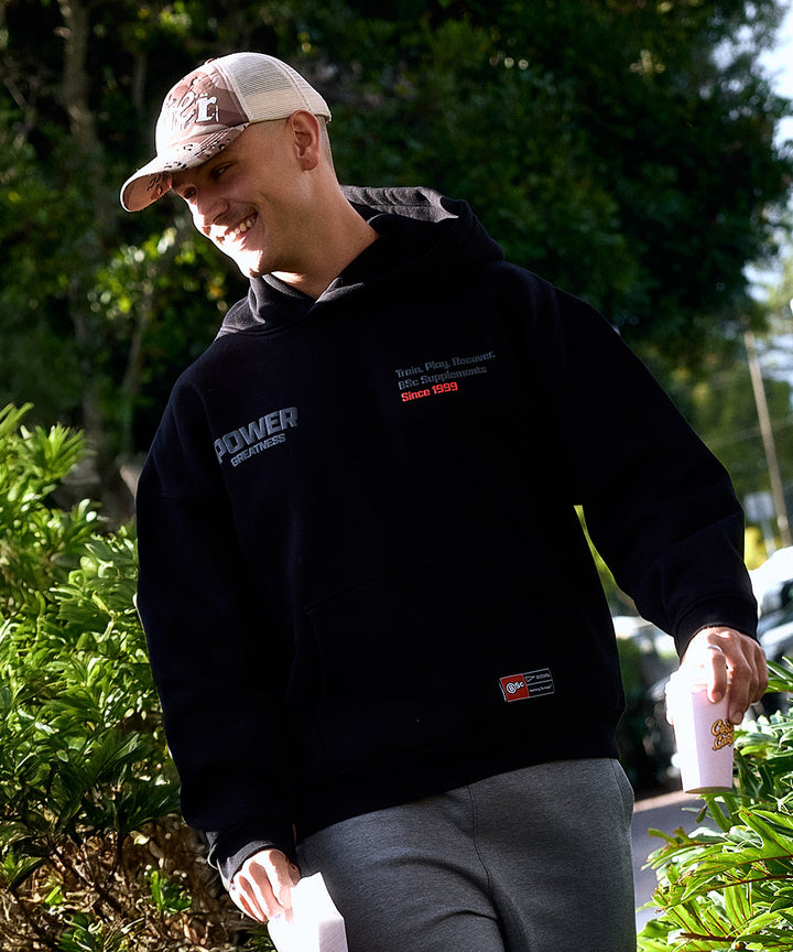 BSc Performance Hoodie in black, worn by a man smiling while holding a coffee cup outdoors